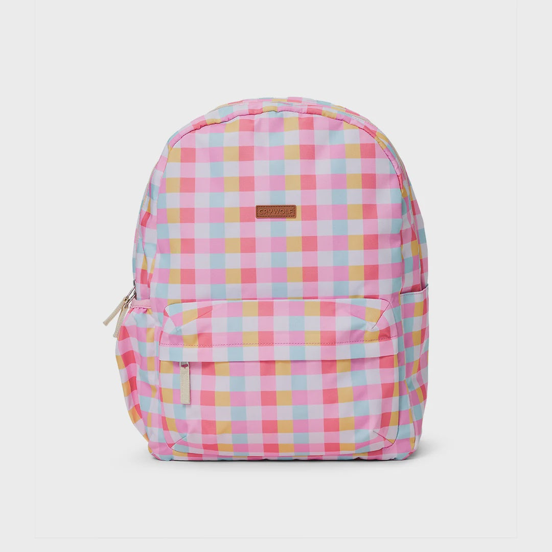 A pink and white gingham patterned backpack with a small brown brand patch on the front, photographed against a light gray background.