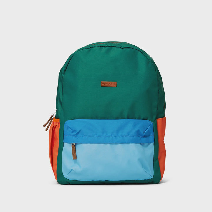 A color-blocked backpack by Jansport, featuring a dark green main body, a bright blue front pocket, a light blue lower front panel, and orange side pockets, shown against a light gray background.
