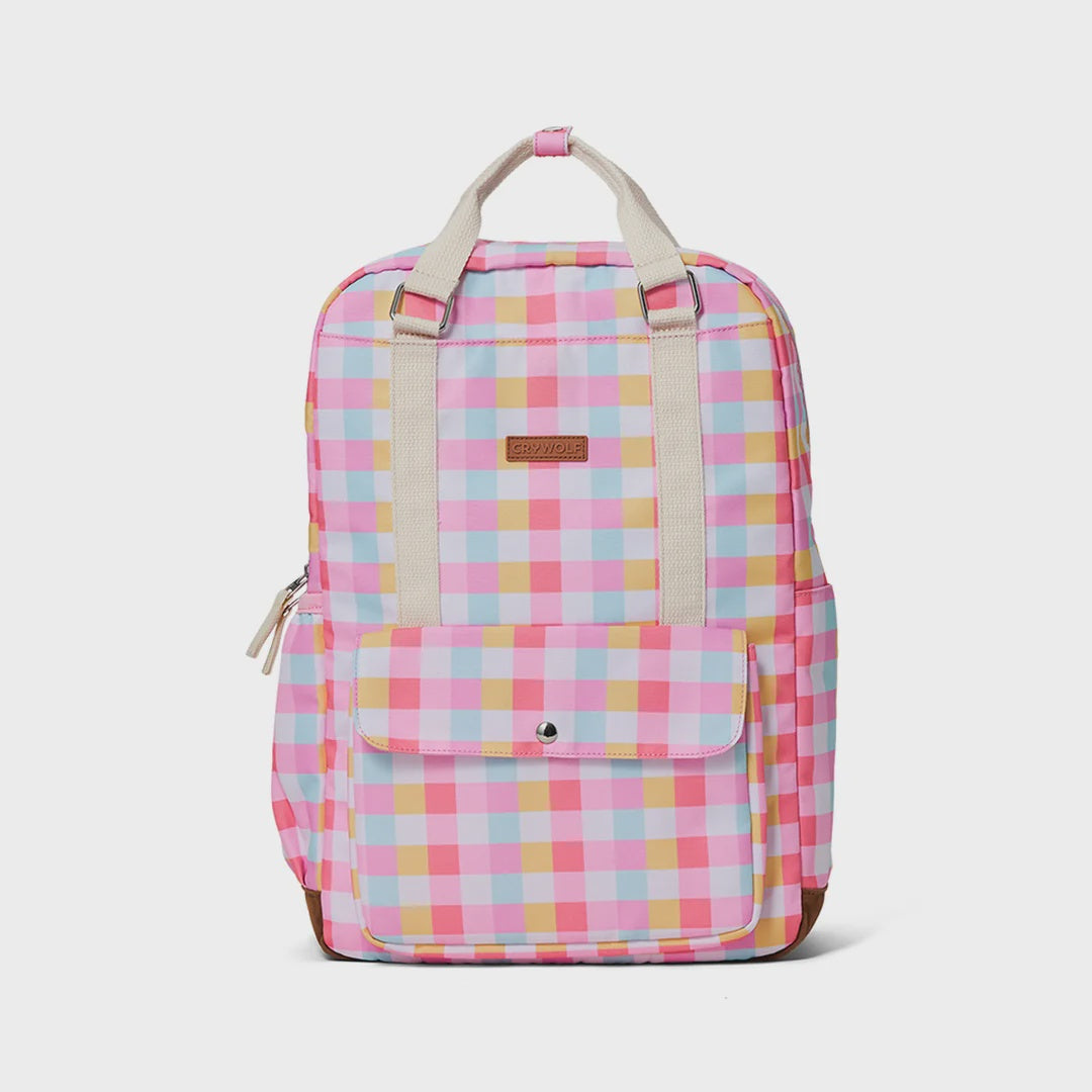 A pastel pink, yellow, and light blue gingham backpack with beige webbing handles and a brown leather brand patch on the front, shown against a light gray background.