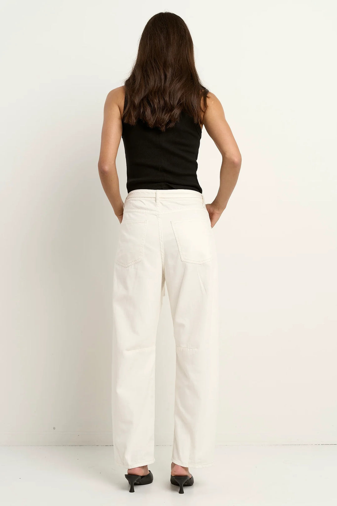 Person wearing a black sleeveless top and white pants on a plain background