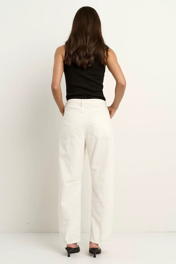 Person wearing a black sleeveless top and white pants on a plain background