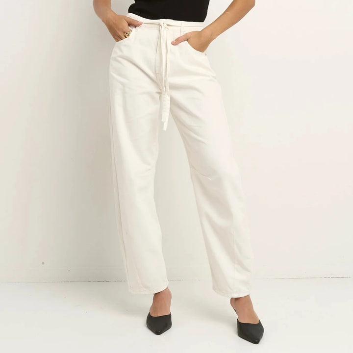 Woman wearing a black sleeveless top and white pants against a white background