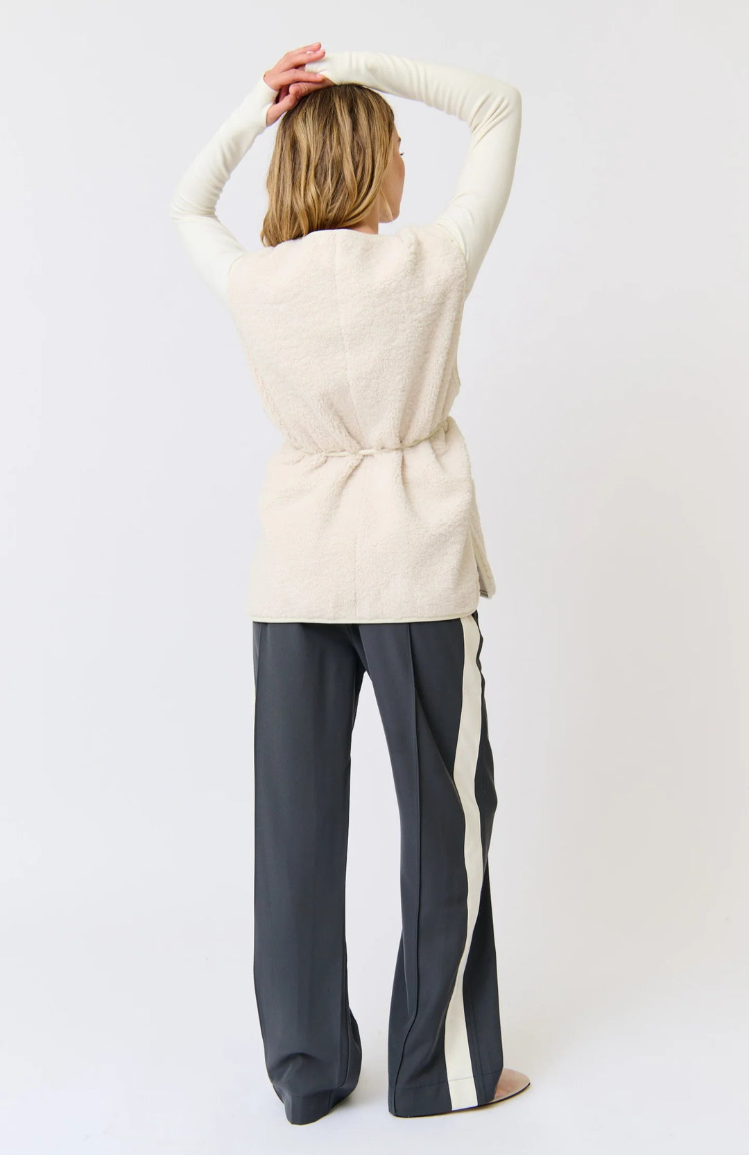 Person wearing a cream cardigan and dark pants against a white background