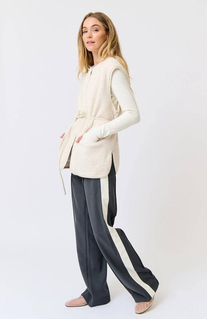 Woman wearing a cream sleeveless top and dark pants with white stripes on a white background