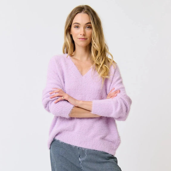 Woman wearing a light purple sweater and blue jeans on a white background