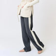 Woman wearing a cream cardigan and dark pants with white stripes on a white background