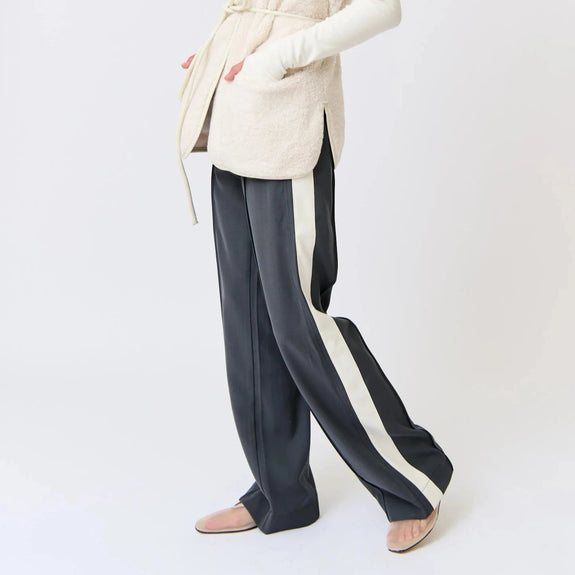Woman wearing a cream cardigan and dark pants with white stripes on a white background