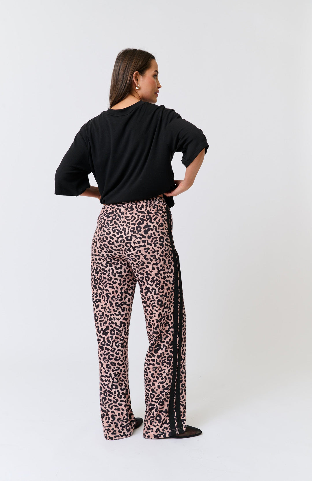 Person wearing a black top and cartel & willow leopard print pants with stripes on a white background