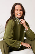 Woman wearing a green sweater with white trim sitting on a white couch.