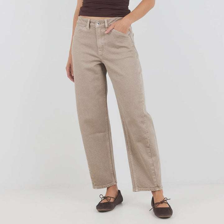 A woman modeling a sleeveless dark brown wrap-style top and beige straight-leg jeans with dark brown flat shoes, standing against a light gray studio background.