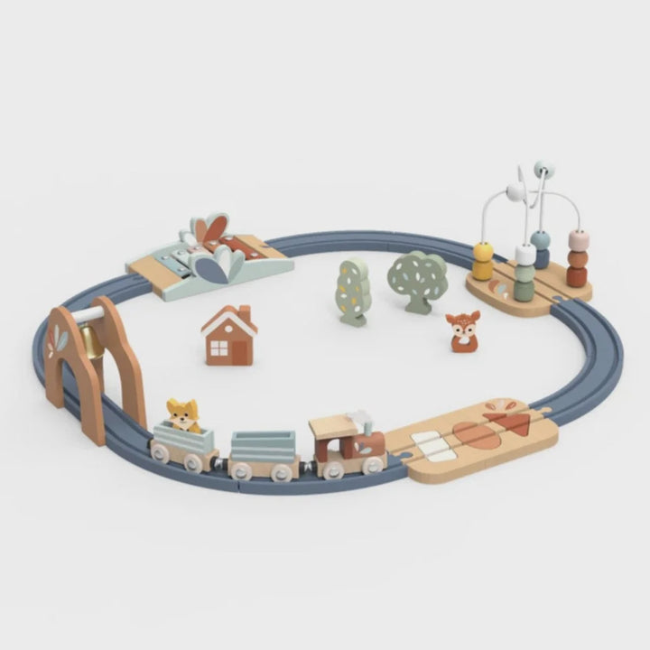 A wooden toy train set arranged in a circular track with a small train, arch bridge, house, trees, and a bead-and-dowel activity board, photographed on a clean light gray background.
