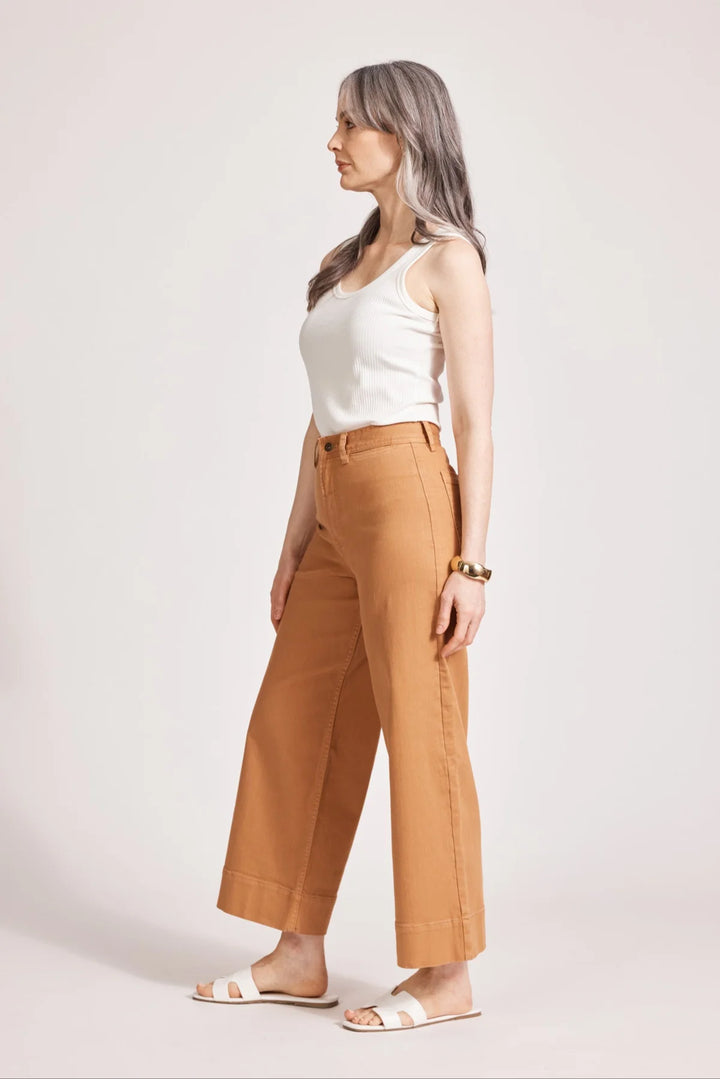Woman wearing a white top and eb and ive tan pants on a plain background