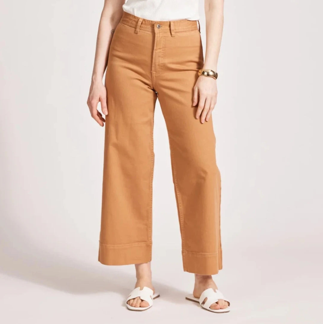 Woman wearing a white tank top and eb & ive brown pants on a light background