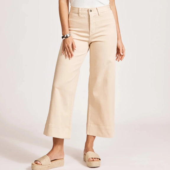 Woman wearing a white sleeveless top and eb & ive beige pants on a light pink background