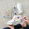 White sneakers with colorful star designs on a textured surface, surrounded by markers.