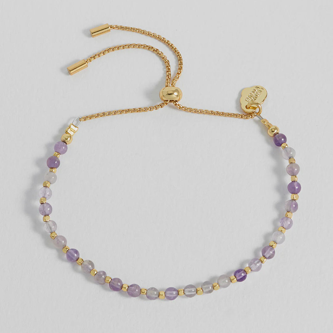 Gold bracelet with purple beads on a light gray background