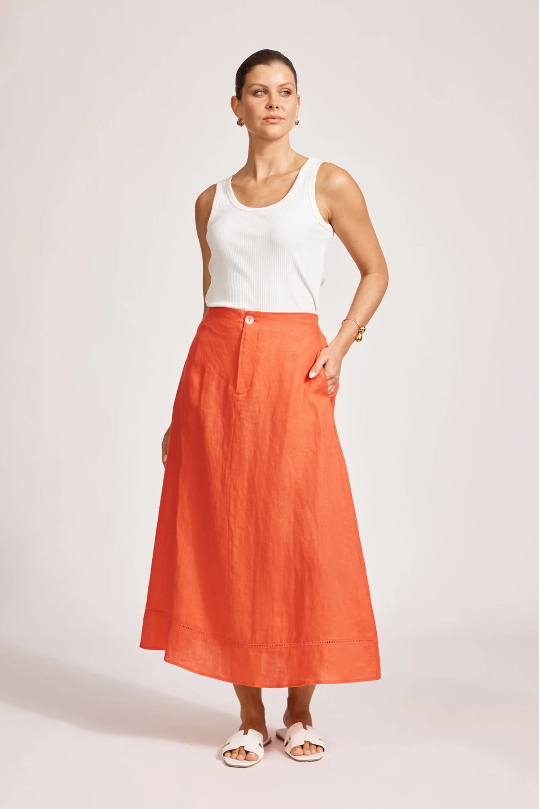 Woman wearing a white sleeveless top and Eb & Ive orange skirt on a light pink background