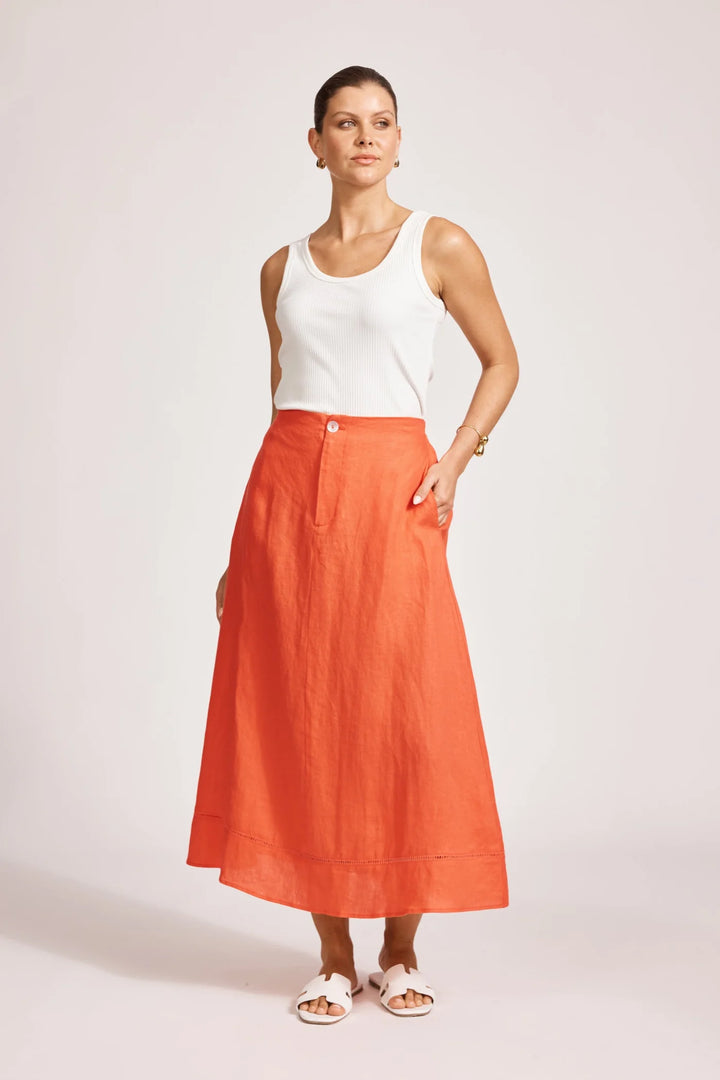 Woman wearing a white sleeveless top and Eb & Ive orange skirt on a light pink background