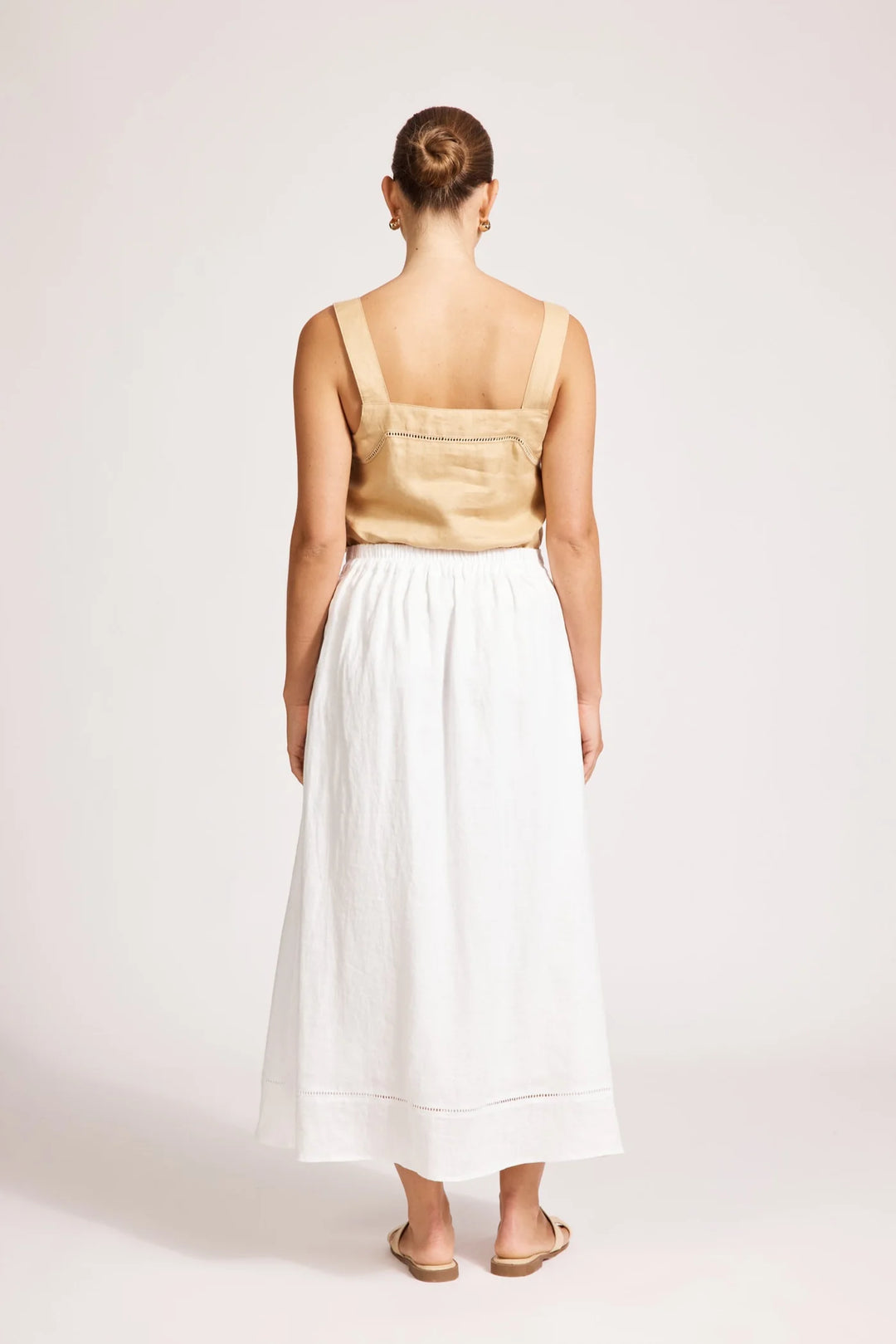 Woman wearing a beige top and white Eb & Ive skirt on a plain background