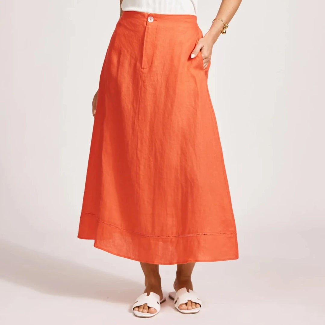 Woman wearing a white sleeveless top and Eb & ive orange skirt on a light pink background