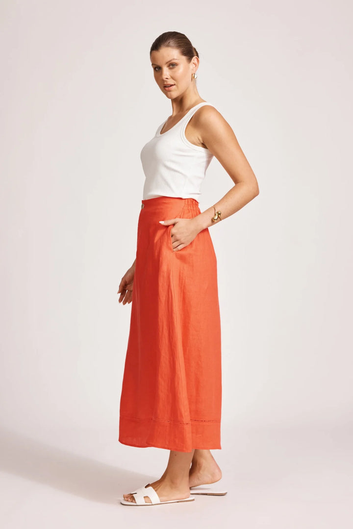 Woman wearing a white top and Eb & Ive orange skirt on a plain background