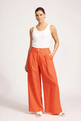 Woman wearing a white sleeveless top and Eb & Ive orange wide-leg pants on a white background