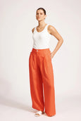 Woman wearing a white tank top and eb & ive orange wide-leg pants on a plain background