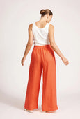 Woman wearing a white top and eb & ive orange pants on a plain background