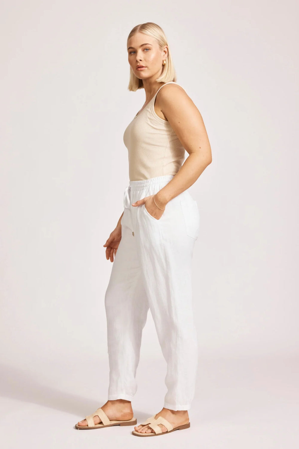 Woman wearing a beige top and eb & ive white pants on a plain background