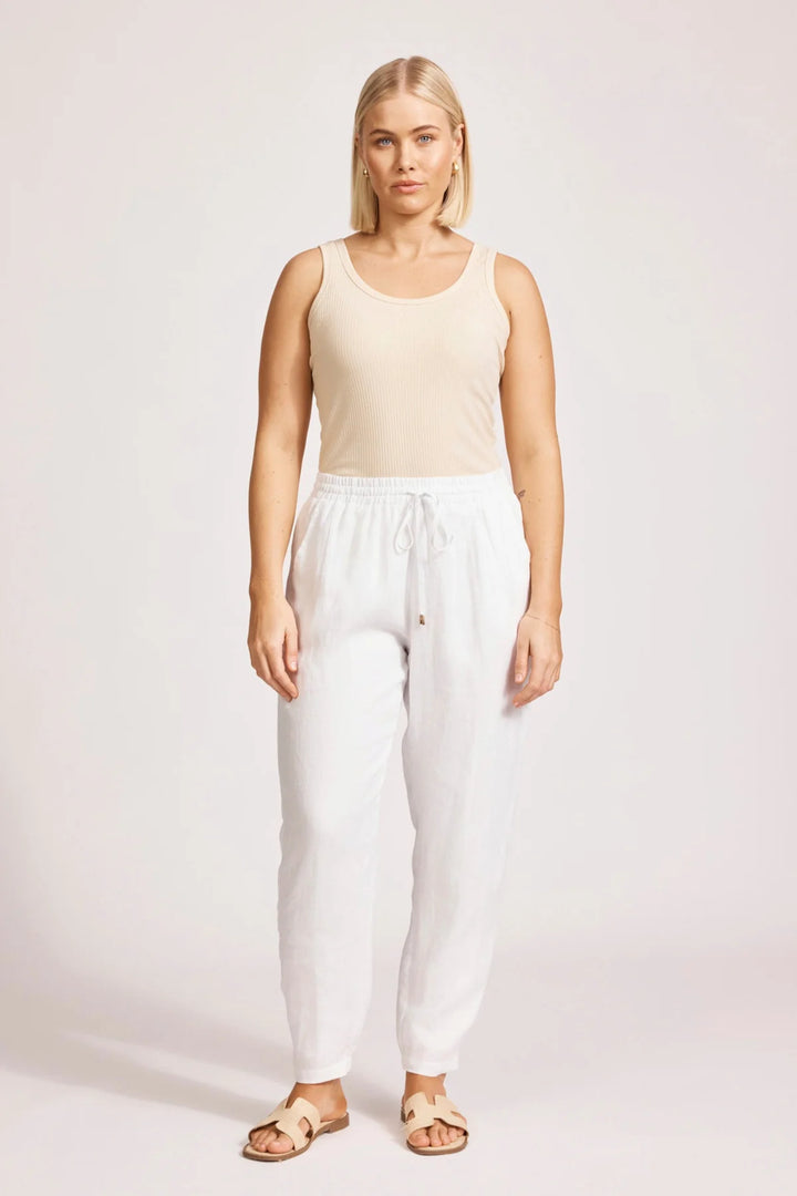 Woman wearing a beige tank top and eb & ive white pants on a plain background