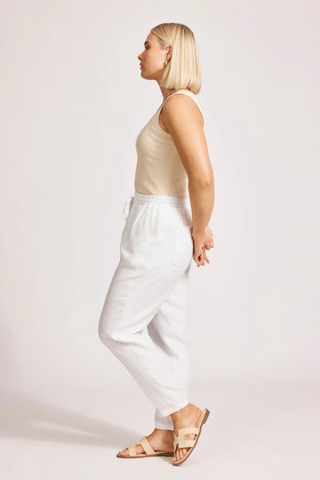 Woman wearing a beige top and eb & ive white pants on a plain background