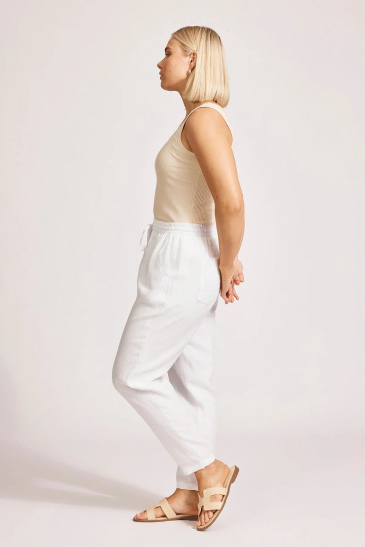 Woman wearing a beige top and eb & ive white pants on a plain background