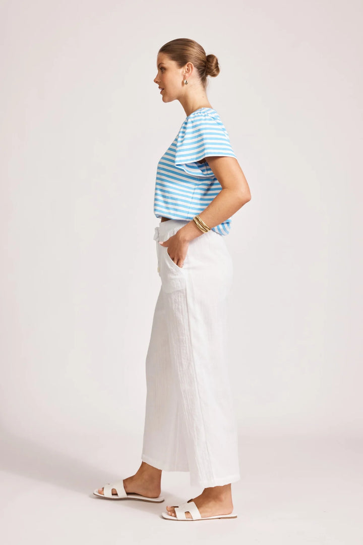 Woman wearing a blue and white striped shirt and Eb & Ive white pants on a light pink background