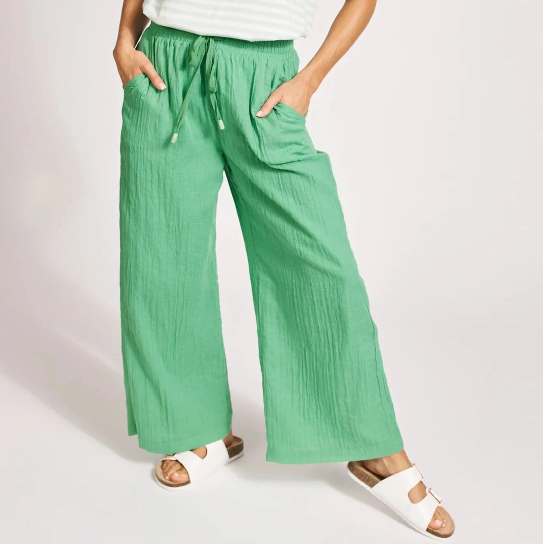 Woman wearing a white striped shirt and Eb & Ive green pants on a light pink background