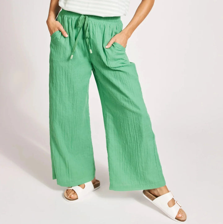 Woman wearing a white striped shirt and Eb & Ive green pants on a light pink background