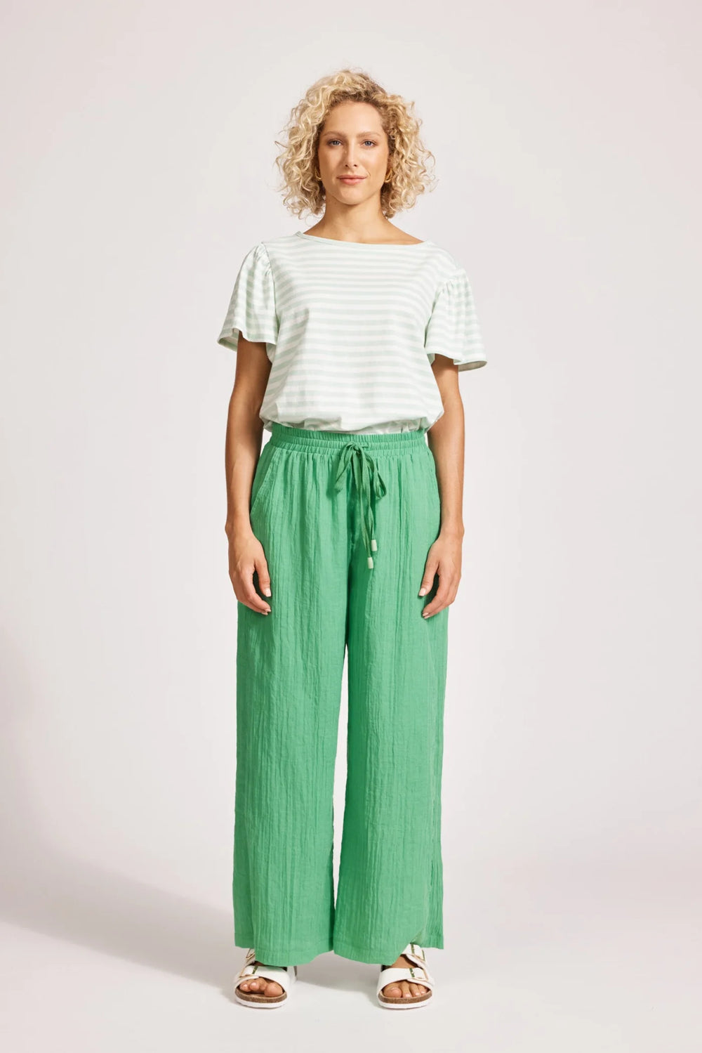 Woman wearing a white top and Eb & Ive green pants on a plain background