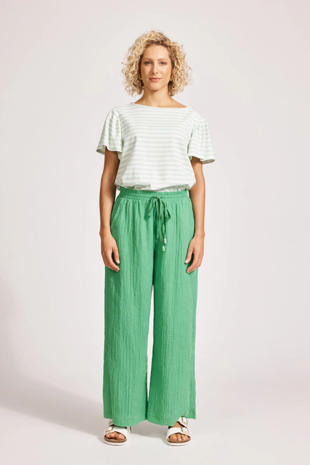 Woman wearing a white top and Eb & Ive green pants on a plain background