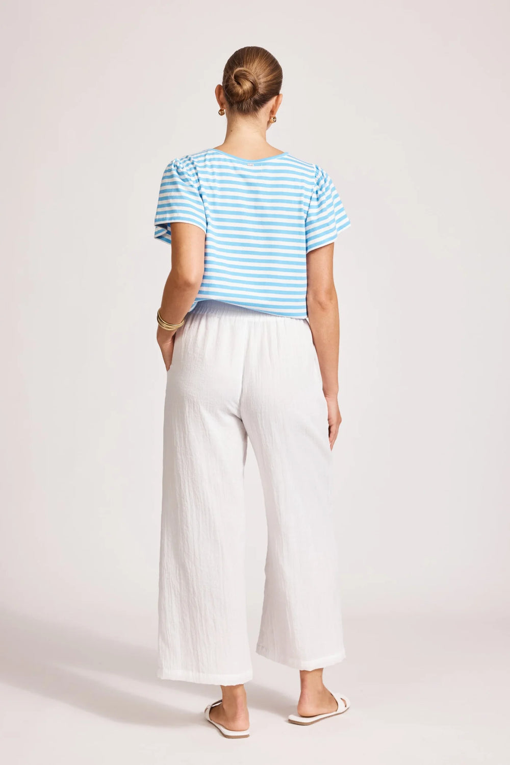 Person wearing a blue striped shirt and Eb & ive white pants on a light pink background