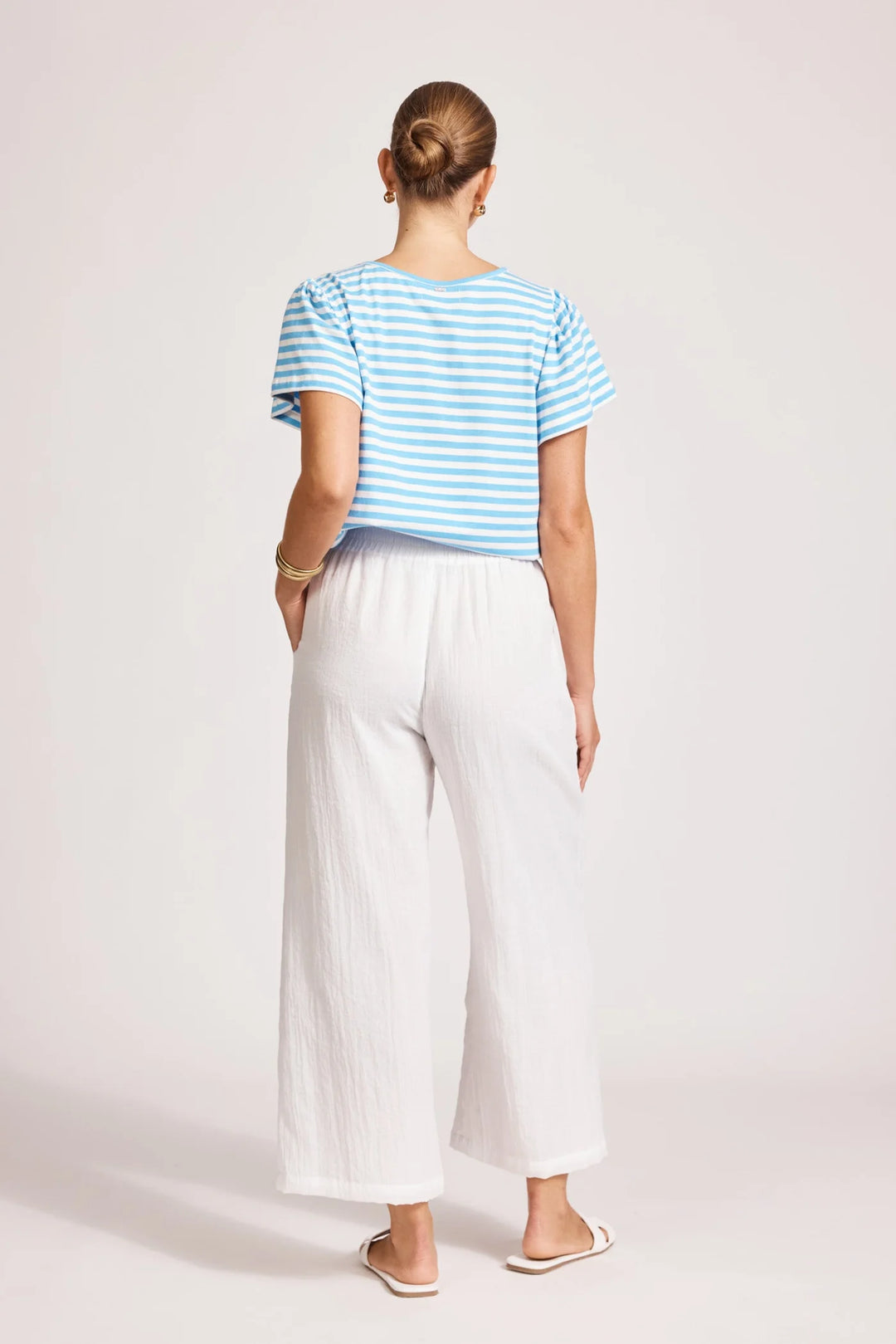 Person wearing a blue striped shirt and Eb & ive white pants on a light pink background