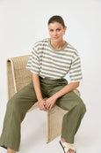 Woman sitting on a wicker chair wearing a striped shirt and green pants against a white background