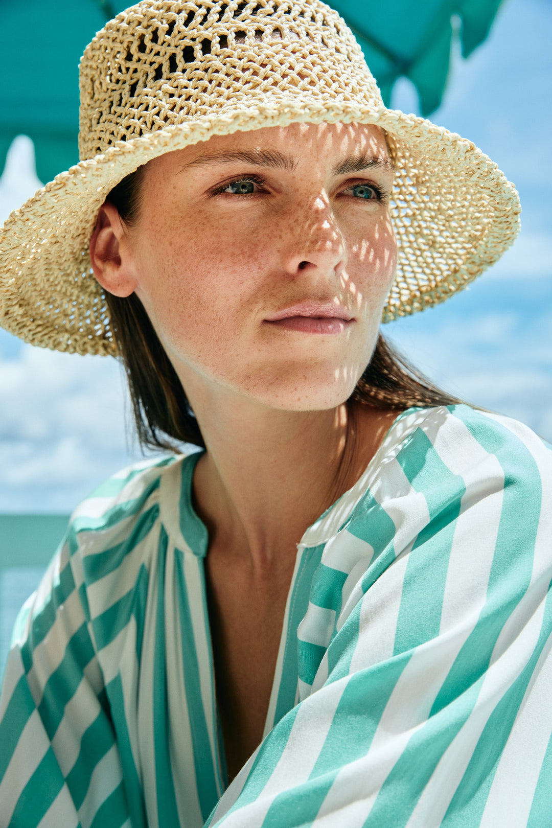 Woman wearing a eb & ive  straw hat and a green and white striped towel on a beach.
