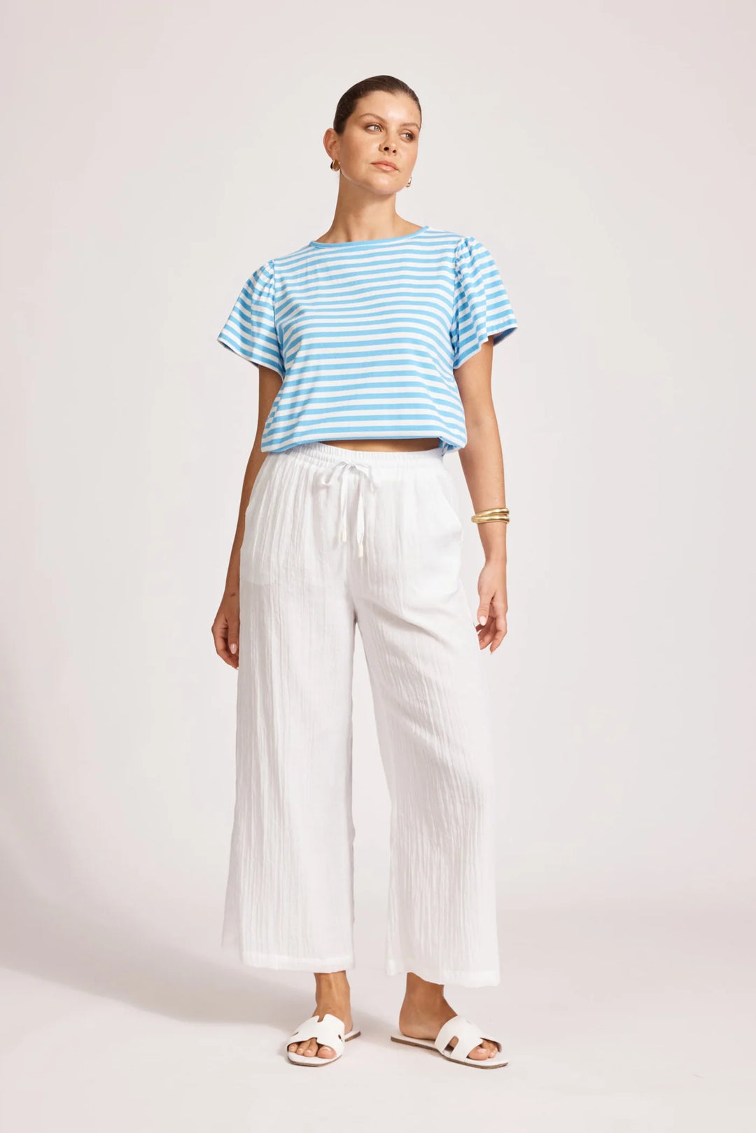 Woman wearing a blue and white striped shirt and Eb & Ive white pants on a plain background