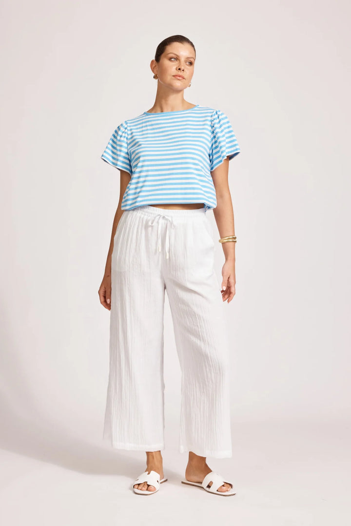 Woman wearing a blue and white striped shirt and Eb & Ive white pants on a plain background