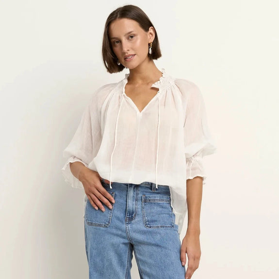 Woman wearing a Among the brave white blouse and blue jeans on a white background