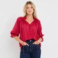 Woman wearing a red among the brave blouse and blue jeans against a white background