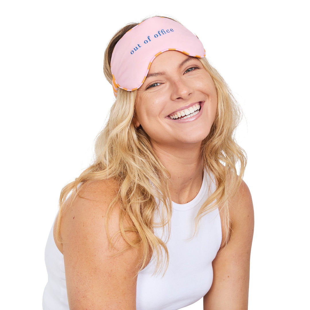 Woman wearing a pink sleep mask with 'out of office' text on a white background