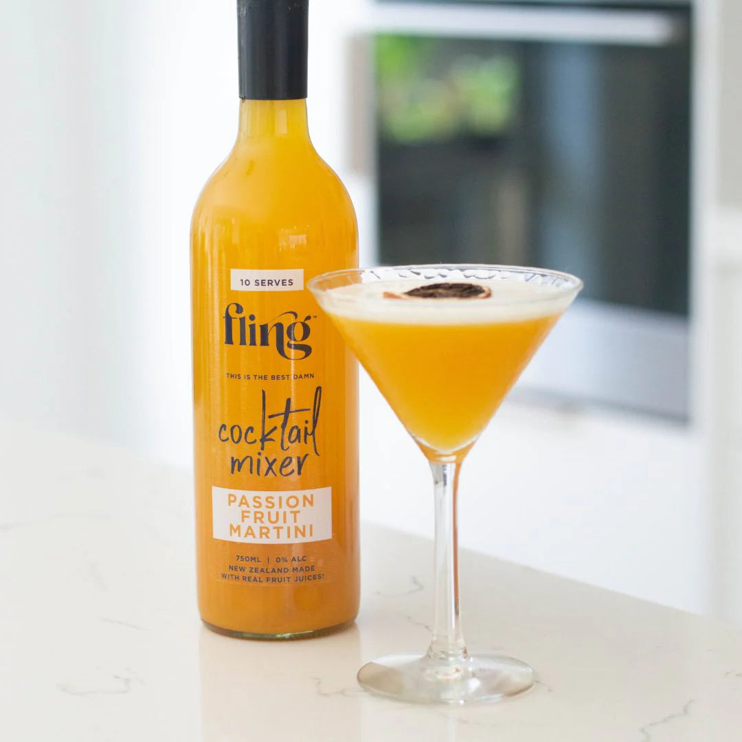 Bottle of Fling cocktail mixer with a glass of orange cocktail on a light surface.