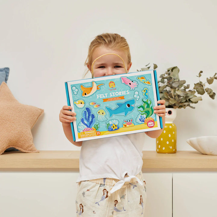 Child holding a felt stories book with colorful illustrations on a wooden shelf.
