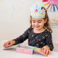 Child wearing a colorful paper crown, sitting at a table with craft materials.