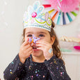 Child wearing a colorful paper crown with bunny ears, holding a purple flower to their nose.